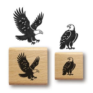 May include: Black eagle illustrations in flight and standing are featured. Two wooden stamps with eagle designs are shown, one with the eagle in flight and the other with the eagle standing. The stamps are made of light-colored wood.