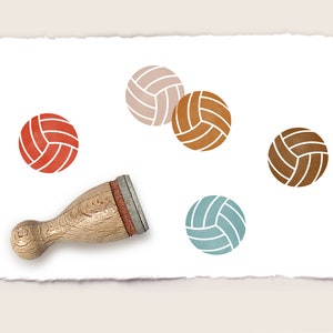 Può includere: Un set di cinque timbri in gomma con diversi disegni di pallavolo colorati. I timbri sono disposti su un foglio di carta bianco con un manico di timbro in legno.