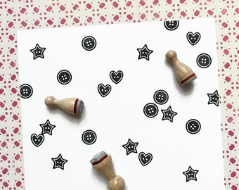 May include: A white sheet of paper with black and white stamps of hearts, stars, and buttons. There are two wooden stamp handles on the paper.