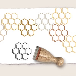 Op de afbeelding: Een wit vel papier met een bruine houten stempel en meerdere honingraatpatronen in goud, bruin, grijs en zwart.