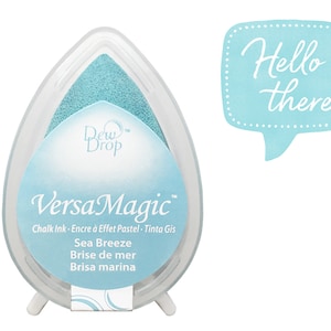 May include: A light blue ink pad with the text "Dew Drop VersaMagic™ Chalk Ink - Encre à Effet Pastel - Tinta Gis Sea Breeze Brise de mer Brisa marina" on the front. The ink pad is in the shape of a teardrop and is sitting on a white stand.