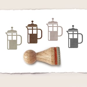 Può includere: Un timbro in gomma di legno con un manico marrone e un design rosso e bianco. Il timbro presenta quattro immagini diverse di una caffettiera a pistone.