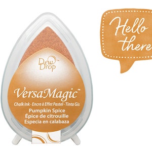 May include: A brown VersaMagic chalk ink pad with the text "Pumpkin Spice" and the words "Épice de citrouille" and "Especia en calabaza" in French and Spanish. The ink pad is in a clear plastic container shaped like a teardrop.