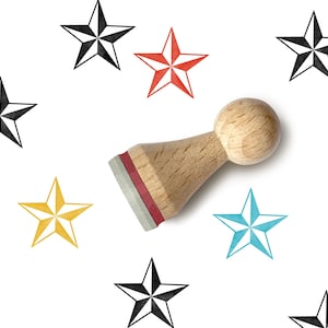 May include: A wooden stamp with a red ink pad is surrounded by star shapes in black, red, yellow, and blue. The stamp has a round wooden handle. The stars are in various sizes and orientations, creating a playful design.