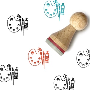 Könnte beinhalten: Ein Holzstempel mit rundem Griff und rotem Kissenboden, platziert über einem sich wiederholenden Muster aus Kunstbedarfs-Symbolen. Jedes Symbol zeigt eine Farbpalette, einen Pinsel und eine Farbtube, die mit der Zahl 2 markiert ist.