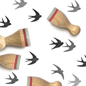 May include: Three wooden stamps with light brown handles and red and gray rubber bases are arranged among several printed black and gray silhouettes of flying swallow birds. The stamps feature a rounded handle design for easy gripping.
