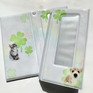 May include: Two white photo albums with clear plastic covers. One album features a kitten and green shamrocks, the other a puppy and shamrocks. Musical notes are also visible. The albums are open, revealing the inside pages.