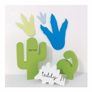 May include: Wooden dinosaur, cactus, and footprint decorations in green, blue, and yellow. The dinosaur is labeled "teddy".