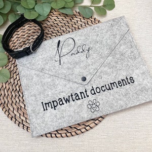 May include: A grey felt folder with the name "Paddy" written in cursive and the text "Impawtant documents" with a paw print icon.
