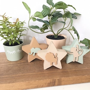 Op de afbeelding: Vier houten stervormige ornamenten met dierensilhouetten. De ornamenten zijn geschilderd in tinten groen, bruin en beige. De dieren omvatten een olifant, een leeuw en een aap.