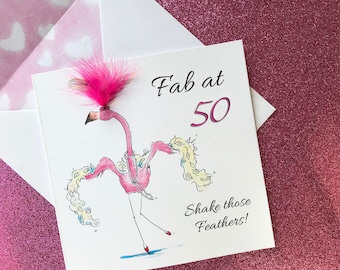 Könnte beinhalten: Ein rosa Flamingo mit einem rosa Federboa und einer rosa Feder auf dem Kopf. Der Flamingo trägt eine Perlenkette und tanzt. Der Text "Fab at 50" und "Shake those Feathers!" steht auf der Karte.