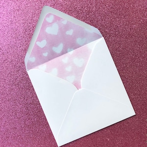 Puede incluir: Un sobre blanco con un forro estampado en rosa y blanco. El forro tiene un dise&ntilde;o de corazones blancos sobre un fondo rosa.