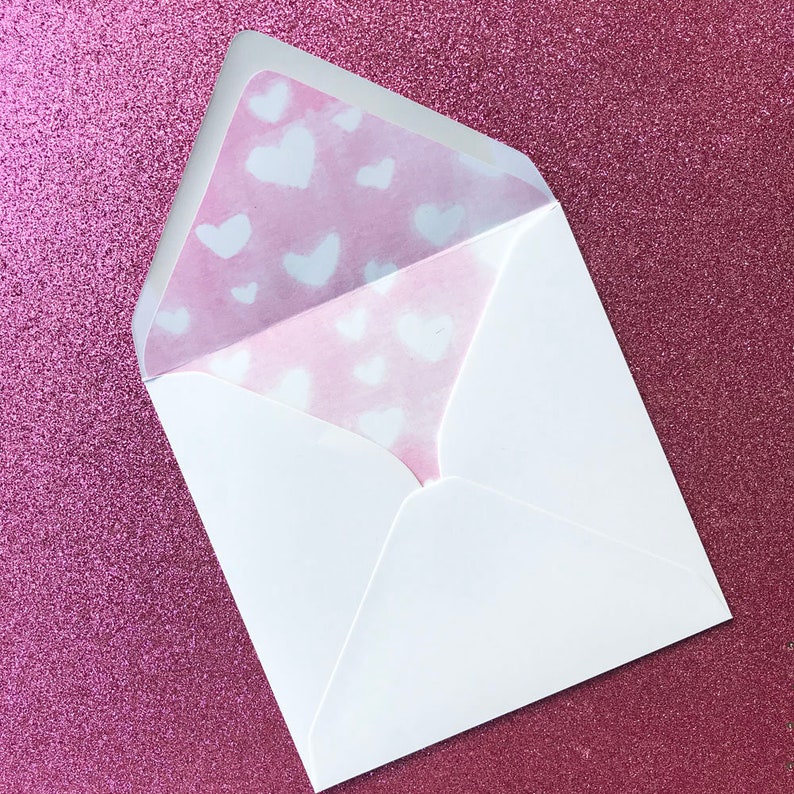Puede incluir: Un sobre blanco con un forro estampado en rosa y blanco. El forro tiene un dise&ntilde;o de corazones blancos sobre un fondo rosa.