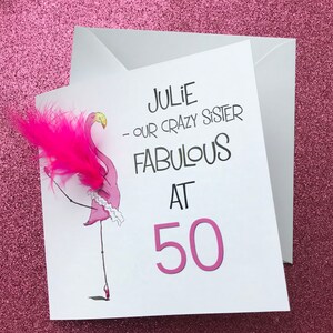 May include: A white card with a pink flamingo illustration and the text "Julie - our crazy sister fabulous at 50".