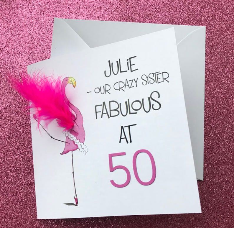 May include: A white card with a pink flamingo illustration and the text "Julie - our crazy sister fabulous at 50".