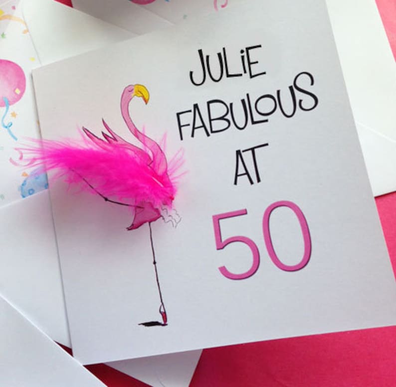 May include: A pink flamingo with a pink feather on its wing, with the text "Julie Fabulous at 50" on a white card.