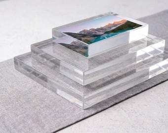 May include: A stack of three clear, rectangular acrylic blocks. The top block features a high-resolution landscape photograph of a mountain range with a turquoise lake, while the two larger blocks beneath it are transparent and empty.