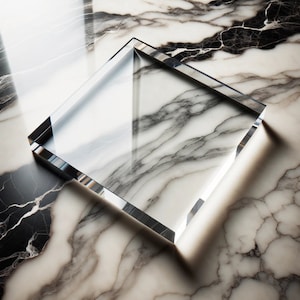 May include: A clear, square glass block with beveled edges. The glass reflects the light and the marble surface beneath it. The marble has a white and gray veined pattern.