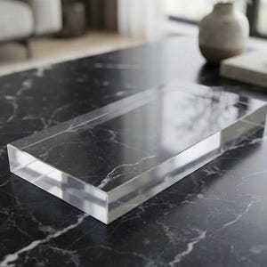 May include: A rectangular clear acrylic tray with a smooth, transparent surface and defined edges. The tray is solid and block-like in construction, featuring a polished finish that reflects light across its flat top and vertical side panels.