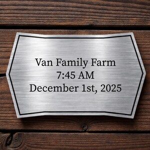 May include: A brushed metal sign with black trim, mounted on a wooden surface. The sign reads "Van Family Farm 7:45 AM December 1st, 2025". The wood has a dark brown color and visible grain.