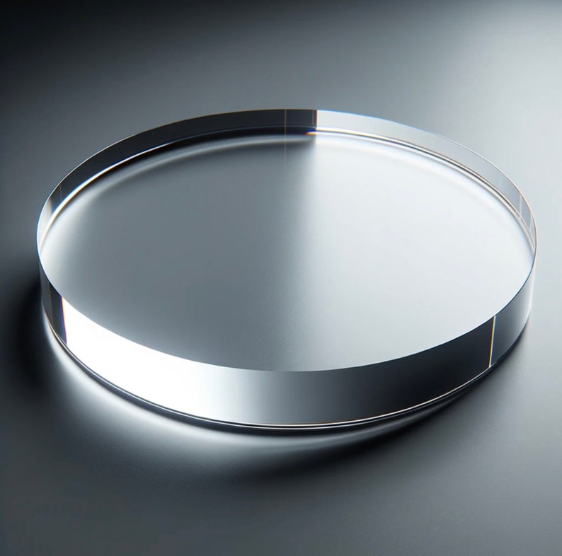 May include: A clear, circular acrylic display stand. The stand is approximately 1 inch thick and has a polished, reflective surface. The edges are smooth and rounded, creating a modern and minimalist aesthetic.