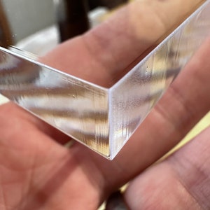 May include: A clear, angled, rectangular object with a reflective surface. The object's corner is in focus, showing a clean, precise edge. The material appears to be glass or a similar transparent substance.