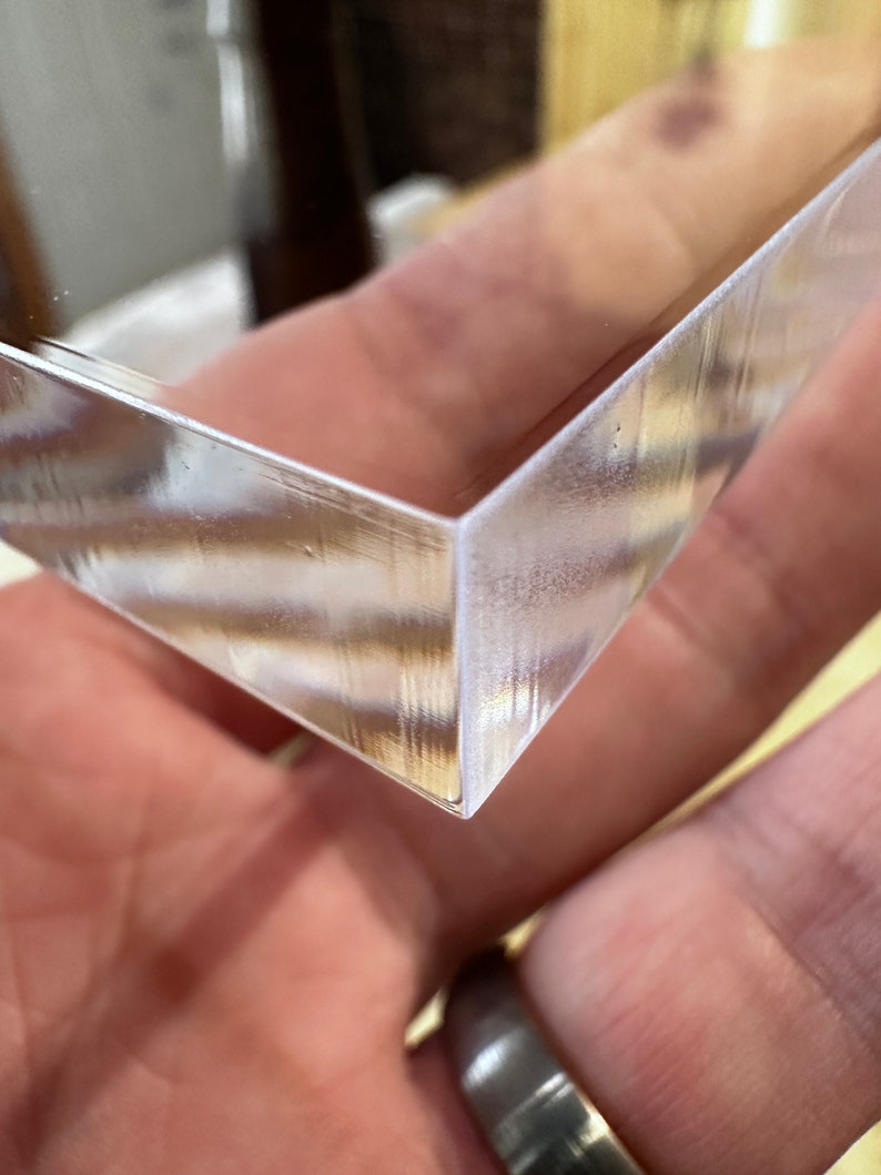 May include: A clear, angled, rectangular object with a reflective surface. The object's corner is in focus, showing a clean, precise edge. The material appears to be glass or a similar transparent substance.