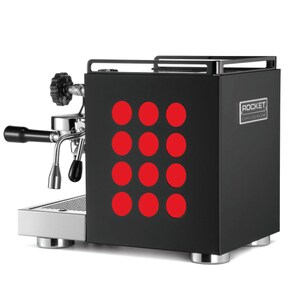 May include: Black espresso machine with a red dot pattern on the front. The machine has a silver portafilter and a silver drip tray. The text "ROCKET" is visible on the front of the machine.