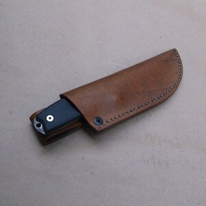 K&ouml;nnte beinhalten: Eine braune Lederscheide mit einem gen&auml;hten Rand und einem schwarzen Messer darin.