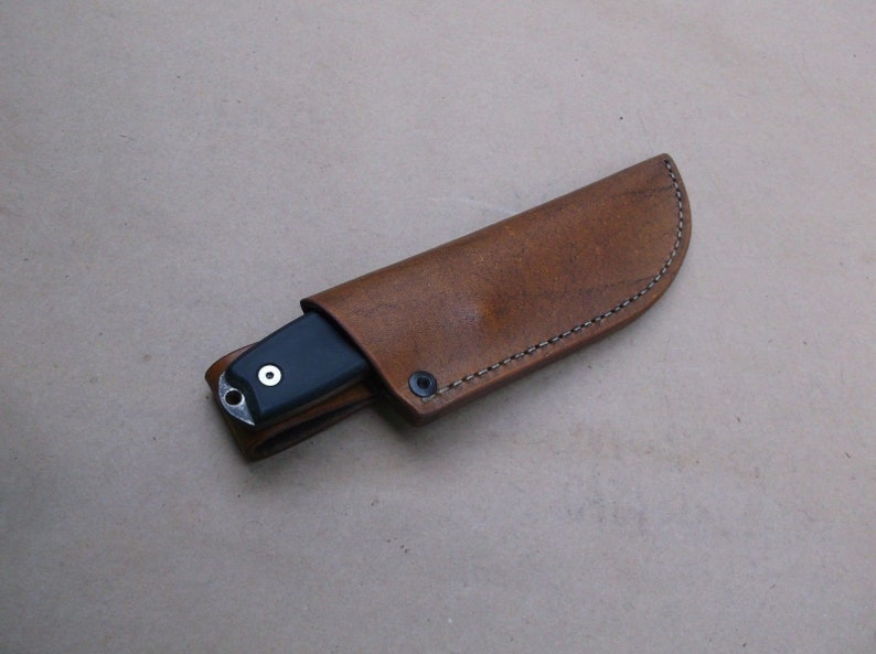 K&ouml;nnte beinhalten: Eine braune Lederscheide mit einem gen&auml;hten Rand und einem schwarzen Messer darin.