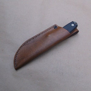 K&ouml;nnte beinhalten: Eine braune Lederscheide mit einem gen&auml;hten Rand f&uuml;r ein Messer.