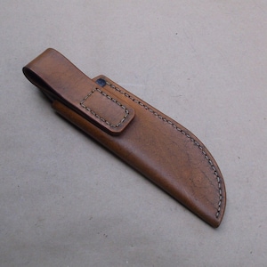 K&ouml;nnte beinhalten: Eine braune Ledertasche f&uuml;r ein Messer mit einem G&uuml;rtelschlaufe und N&auml;hten.