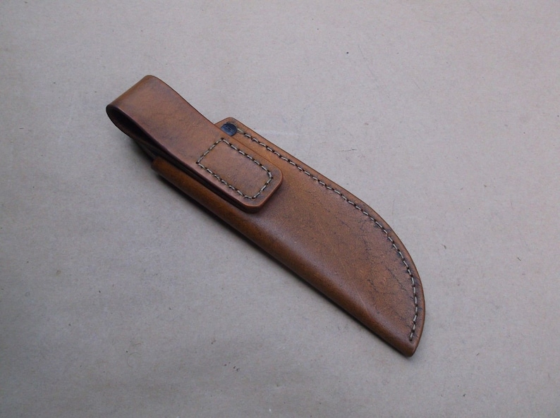 K&ouml;nnte beinhalten: Eine braune Ledertasche f&uuml;r ein Messer mit einem G&uuml;rtelschlaufe und N&auml;hten.