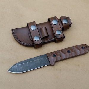 May include: A brown leather sheath with a metal snap closure and a brown handled knife with a black blade. The knife has the word "ESEE" printed on the blade.