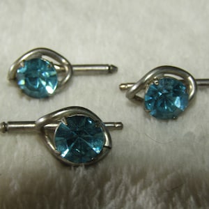 May include: Three silver tie tacks with blue gemstone accents. Each tack features a twisted design.