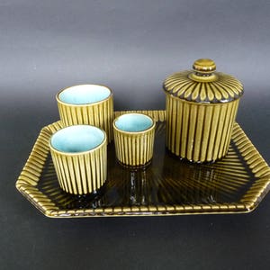 Puede incluir: Un juego de cuatro tazas de cerámica marrón y verde y un tarro con tapa en una bandeja a juego. Las tazas tienen un interior azul claro.