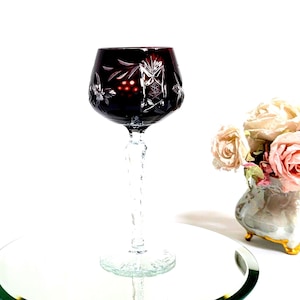 May include: A dark red crystal wine glass with a cut design. The glass has a long, twisted stem and a round base.