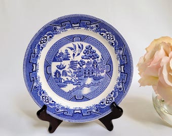 Puede incluir: Un plato de porcelana azul y blanco con un diseño de sauce. El plato está en un soporte de madera.