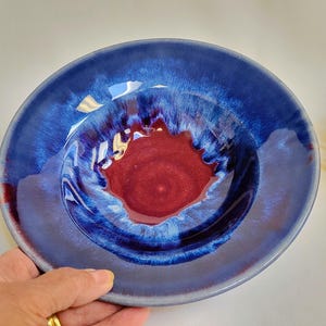 May include: A blue and red ceramic bowl with a swirling glaze pattern. The bowl is handmade and has a unique, artistic design.