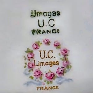 May include: A white ceramic surface featuring a maker's mark with the text Limoges U.C. FRANCE. Below this, a circular wreath of pink roses and green leaves surrounds the text U.C. Limoges, with the word FRANCE printed at the bottom.