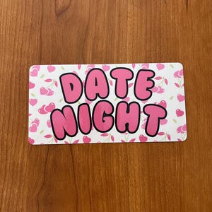 May include: A white rectangular sign with a pink cherry pattern. The sign says "DATE NIGHT" in large pink bubble letters.