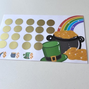 May include: A white card with a rainbow, a pot of gold, and a leprechaun hat. There are 25 gold circles on the card, each with a dollar sign.