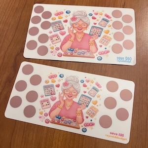 May include: Two white bingo cards with a cartoon illustration of a smiling elderly woman wearing glasses and holding bingo cards. The cards have pink circles and the text "save $60 reynoldsbudget" and "save $25 reynoldsbudget".