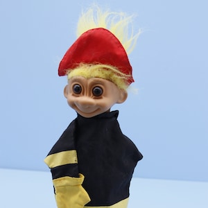 Puede incluir: Un títere de troll de pelo amarillo que lleva un sombrero rojo y un traje de bombero negro y amarillo.