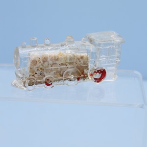 May include: A clear glass toy train with red wheels. The train is on a clear glass surface.