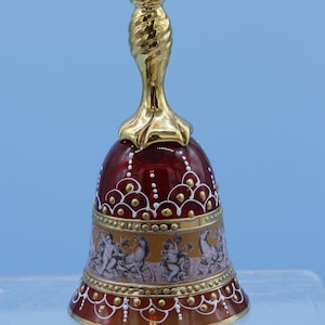 Puede incluir: Una campana de vidrio roja con una parte superior pintada en oro y diseños intrincados pintados en blanco y oro. La campana presenta una escena con figuras y caballos.