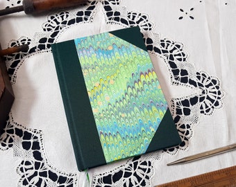May include: A green hardback journal with a marbled paper cover in shades of green, blue, and yellow. The marbled paper is on the front and spine of the journal.
