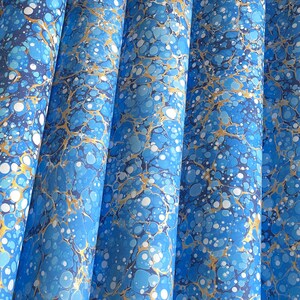 Könnte beinhalten: Nahaufnahme mehrerer Papierrollen mit Marmormuster. Das Papier weist Blau-, Weiß- und Goldtöne auf und erzeugt ein wirbelndes, strukturiertes Muster. Die Rollen sind vertikal angeordnet und zeigen die komplizierten Details des Designs.