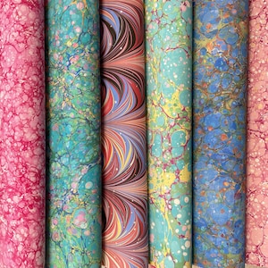 May include: A collection of eight rolls of decorative paper with marbled patterns in shades of blue, pink, and green. The paper has a textured, almost bubbly appearance.