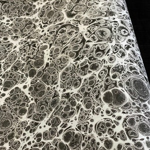 Pode incluir: Papel marmorizado abstrato em preto e branco com um padrão de linhas brancas e círculos pretos que se entrelaçam.